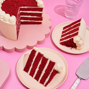 Red Velvet Cake with four moist layers and cream cheese frosting, served on pink plates with a glass of water.